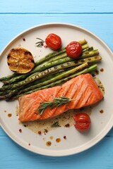 Tasty grilled salmon with tomatoes, asparagus and spices on light blue wooden table, top view