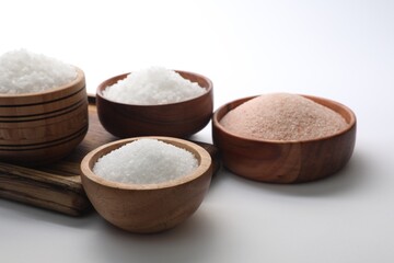 Different types of natural salt in wooden bowls on white background
