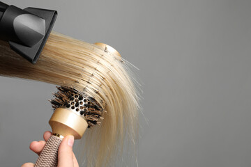 Hairdresser blow drying client's hair on light grey background, closeup. Space for text - obrazy, fototapety, plakaty