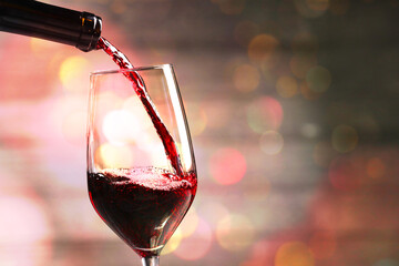 Pouring red wine into glass against background with blurred lights, closeup. Space for text