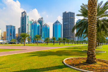 The skyline of downtown Sharjah from the waterfront Corniche Central Souq Park along Khalid Lake at Al Majaz Waterfront, Sharjah, United Arab Emirates. - obrazy, fototapety, plakaty