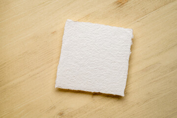 small, square, blank sheet of watercolor paper against wooden background