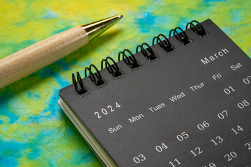 March 2024 - small spiral desktop calendar with a stylish pen against colorful marbled paper, time and business concept