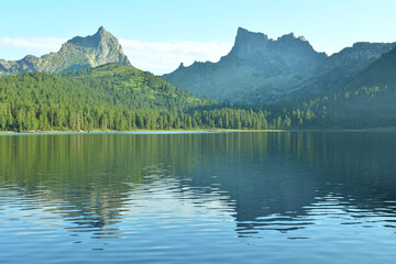 Reflection of two high pointed rocks in a large lake with shores covered with a dense cedar forest,...