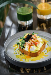 Delicious toast with egg Benedict or poached egg, black caviar, shrimps and microgreens on plate on marble table with smoothies. Healthy breakfast food, diet, top view