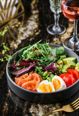 Buddha bowl salad with salmon fish, arugula, spinach, avocado, tomatoes, green edamame beans, eggs on marble background. Healthy salad, dieting, top view, close up