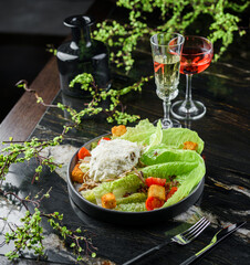Fresh vegetable salad with grilled chicken meat, cherry tomatoes, lettuce, crouton and sauce on dark marble table with drinks. Caesar salad, healthy food, top view