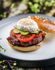 Beef burger with poached egg or Eggs Benedict, tomatoes, cucumbers, sauce and fried meat cutlet on...