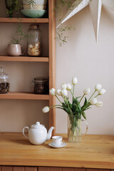 Fototapeta na wymiar Stylish interior of a wooden Scandinavian kitchen. Fresh flowers in a vase. Ceramic plates, dishes, utensils and cozy decor on wooden shelfs. Open shelves in the kitchen. 