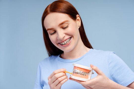 Image of a smiling, attractive redhead woman demonstrating a tooth model cleaning with floss holder