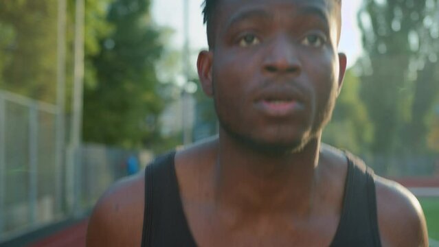 African American ethnic man guy runner jogger sprinter running on race track outdoor stadium sport ground determined male jogging morning workout run jog exercise outside city fast motion motivation