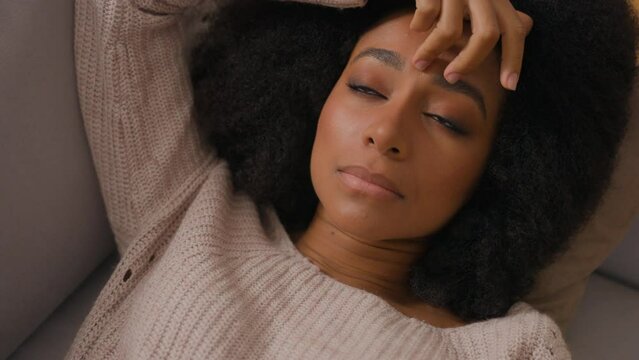 Lonely sad depressed African American woman lying on couch alone at home unhappy apathetic tired lazy girl female relaxing on sofa depression suffering from psychological problem mental think pensive 