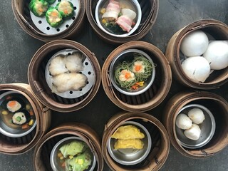 top view shot of many kind of chinese style steamed dim sum dishes in bamboo baskets on gray table