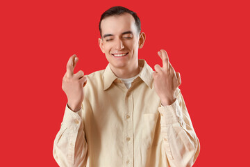 Young man crossing fingers on red background