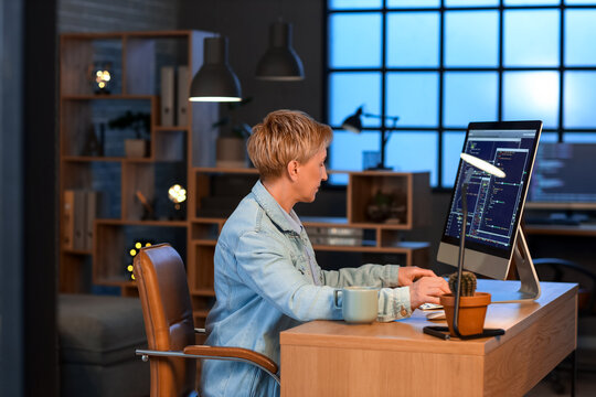 Mature female programmer working with computer in office at night