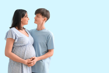 Fototapeta premium Young expectant couple embracing pregnancy journey, future parenthood, and family planning on a light blue background