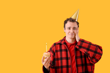 Sad young man with birthday cake on yellow background
