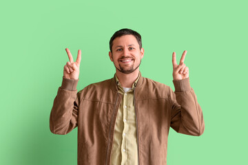 Handsome man showing victory gesture on green background