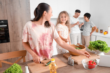 Happy mother with her little daughter cooking vegetable salad in kitchen