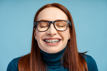 Ginger haired woman with brackets and specs, standing with her eyes closed and a joyful smile