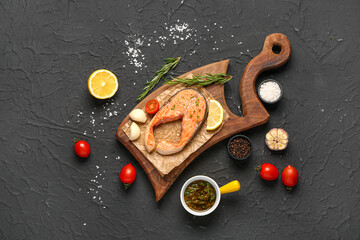 Wooden board of tasty salmon steak with tomatoes, garlic and lemon on black background