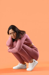 Beautiful young afraid woman sitting on orange background