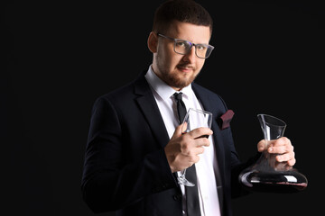 Young sommelier with decanter and glass of wine on black background