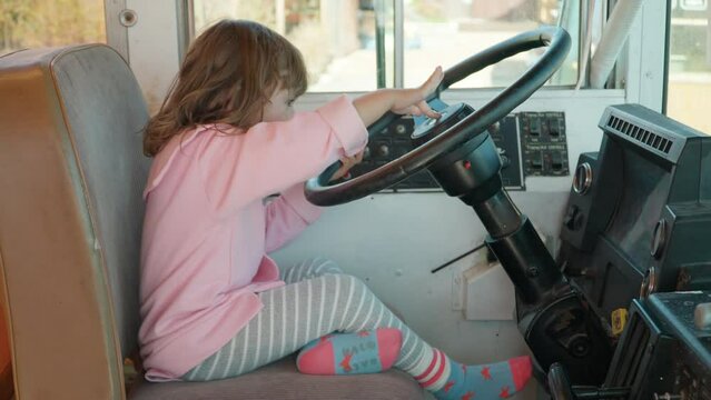 Adorable Child in Old Bus Driver's Seat Pretends to Drive Turning Steering Wheel Rapidly and Pressing Beep Signal - side view