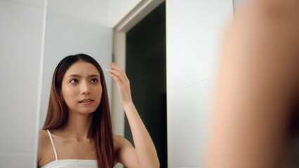 Proud and Happy moment of Attractive asian woman touching and comb hair healthy hair or hair coloring looking at mirror in bathroom. Young pretty female enjoying her beauty routine hair treatment.