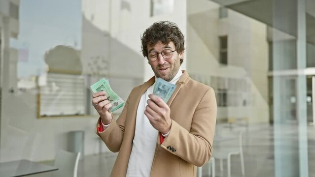 Handsome man counting malaysian ringgit on a city street, surrounded by urban architecture.