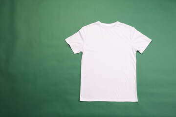 A plain white t-shirt is laid out flat against a green background, with copy space