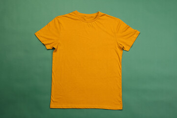 A plain yellow t-shirt is laid out flat against a green background, with copy space