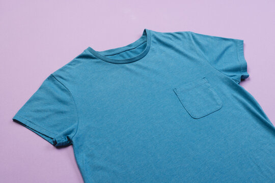 Fototapeta A plain blue t-shirt with a pocket is laid out on a purple background, with copy space