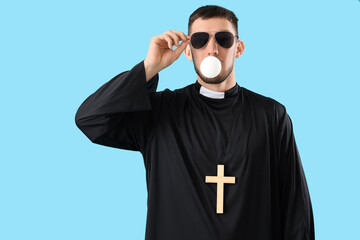 Cool young priest chewing gum on blue background