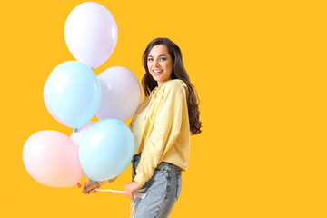 Fototapeta na wymiar Pretty young woman with balloons celebrating birthday on yellow background