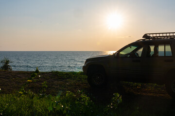 Fototapeta premium Phuket Thailand January 22,2024:Brown American SUV Jeep Grand Cherokee WJ 2002 on the beach sunset sky background in Phuket island Thailand,Travel and camping concept transportation background