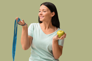 Beautiful young woman with fresh apple and measuring tape on green background. Weight loss concept