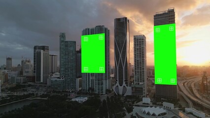 Aerial of smart city skyline at sunset with empty billboard green screen with tracking markers on modern buildings skyscraper