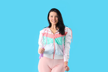 Sporty young woman with skipping rope on blue background