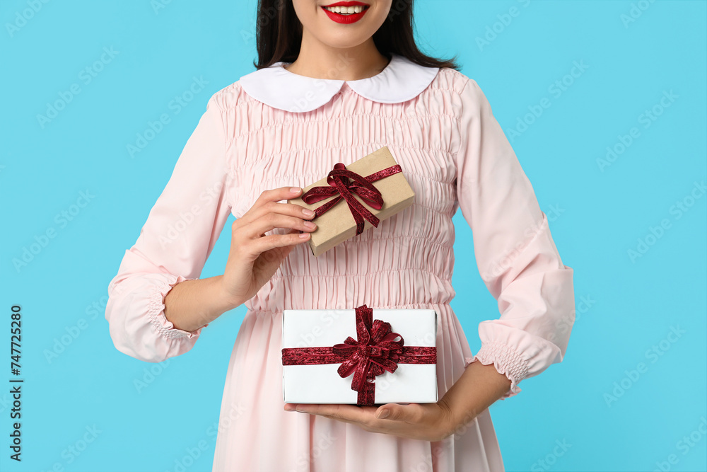 Wall mural Beautiful young woman with gift boxes on blue background. Valentine's Day celebration