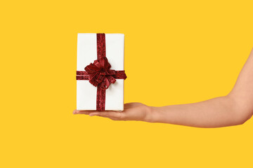 Female hand with gift box on yellow background. Valentine's Day celebration