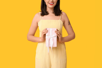 Beautiful young happy woman with gift box on yellow background. Valentine's Day celebration