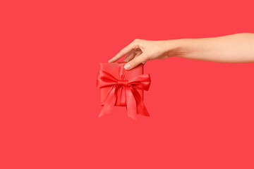 Female hand with gift box on red background. Valentine's Day celebration