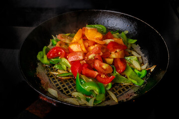 Stir-fried tomatoes and bell peppers in an iron pan.