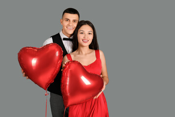Fototapeta na wymiar Young couple with heart-shaped air balloons for Valentine's day on grey background