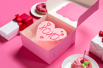 Heart-shaped bento cake with gift boxes, cupcake and donut on pink background. Valentine's Day celebration