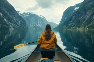 Foto op Canvas Rear view of a young woman paddling a canoe through calm waters Surrounded by majestic fjords Capturing a moment of solitude and adventure © Bijac