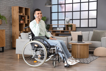 Happy young man in wheelchair talking by mobile phone at home