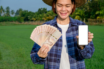Thai banknotes money with blank screen smartphone are held by female farmers at green farms.