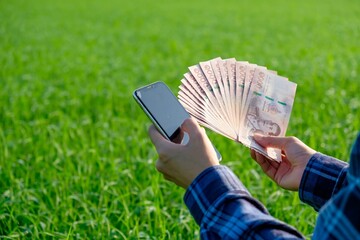 Thai banknotes money with blank screen smartphone are held by female farmers at green farms.